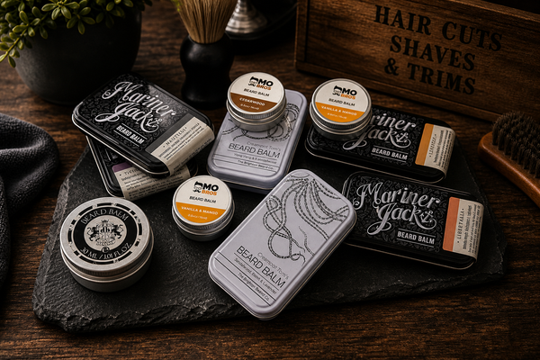 Selection of premium beard balms and men’s grooming products displayed on dark slate and rustic wood with warm vintage barbershop styling.