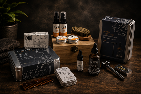 Men’s grooming gift sets and shaving kits arranged on a dark wooden surface with beard care products, shave oil, razor and grooming accessories in a warm moody studio setting