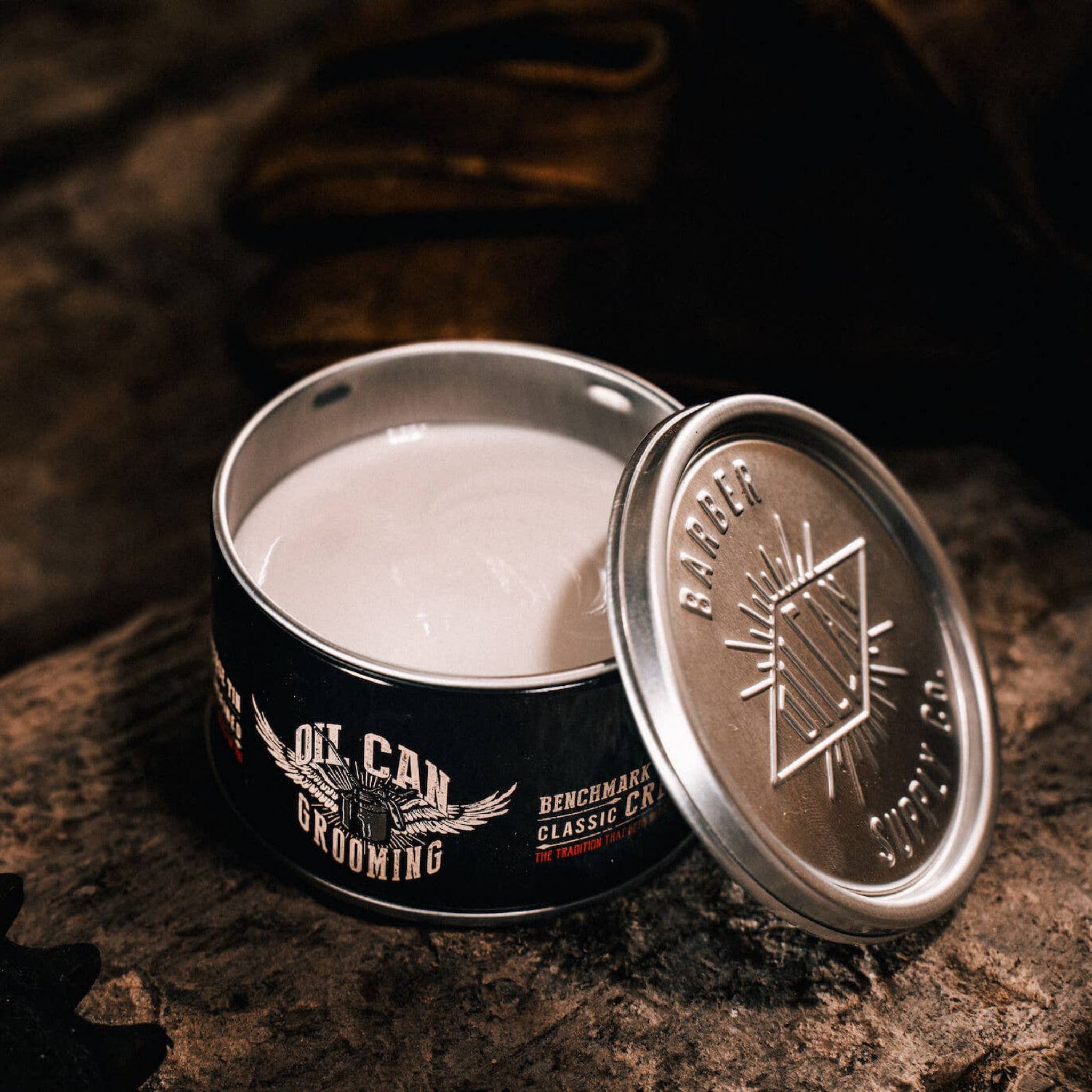 Oil Can Grooming's Benchmark Classic Hair Cream open tin on rustic wooden surface with vintage barbershop styling accessories