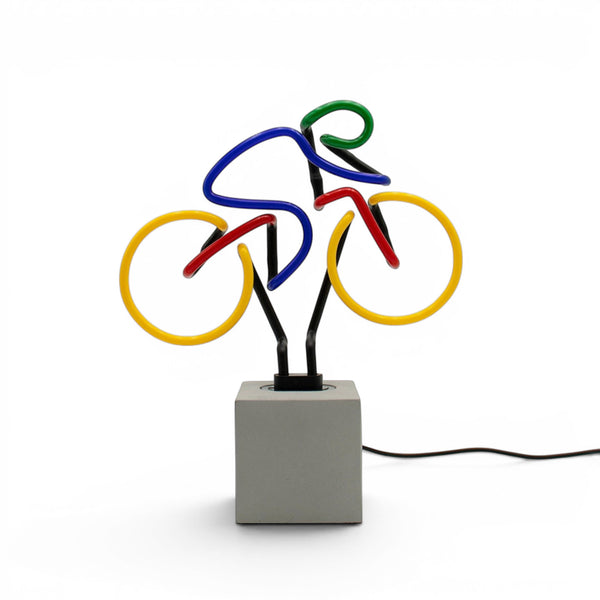 Multi coloured bicycle neon lamp on concrete effect base with visible power cable against white background