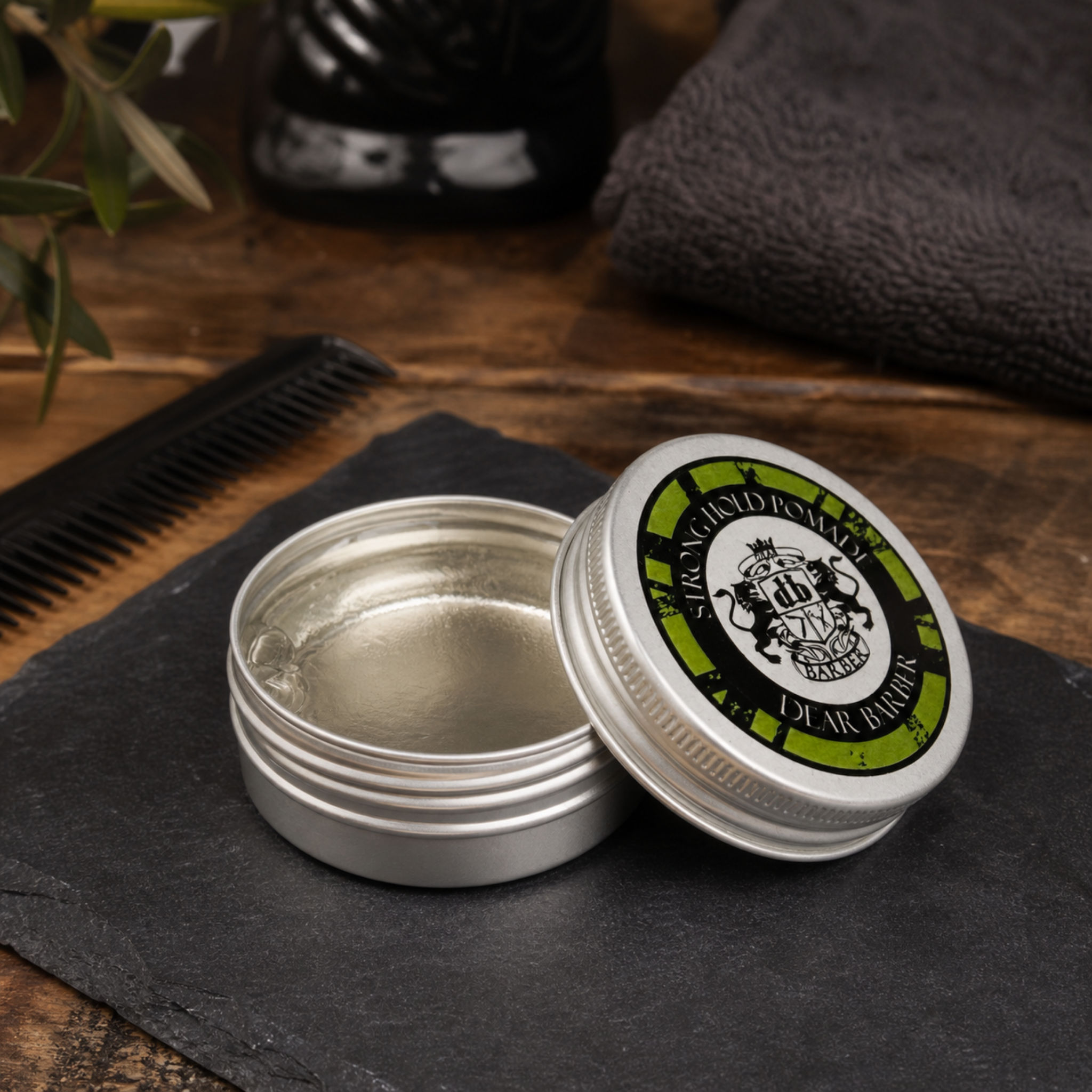 Dear Barber Strong Hold Pomade 20ml open styling pomade tin in a classic barber shop lifestyle scene with comb and grooming accessories