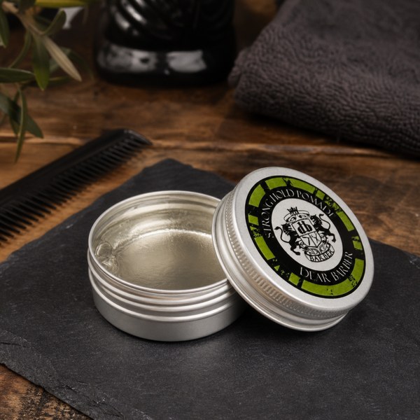Dear Barber Strong Hold Pomade 20ml open styling pomade tin in a classic barber shop lifestyle scene with comb and grooming accessories
