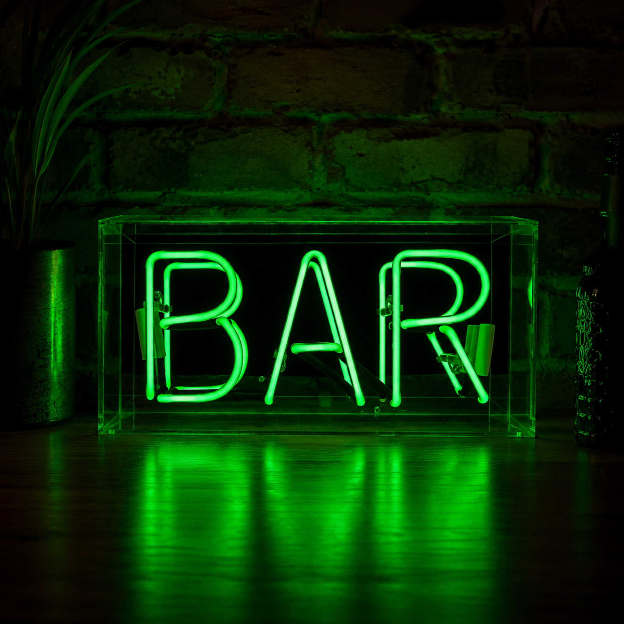 Green BAR neon sign glowing on a wooden surface with dark brick wall background and green light reflections