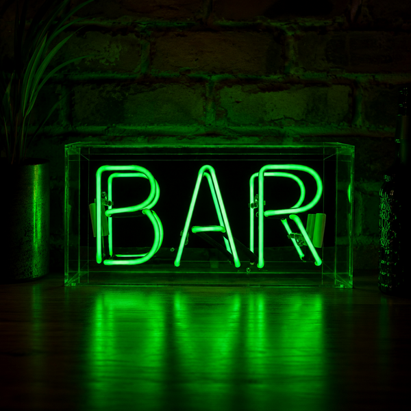 Green BAR neon sign glowing on a wooden surface with dark brick wall background and green light reflections