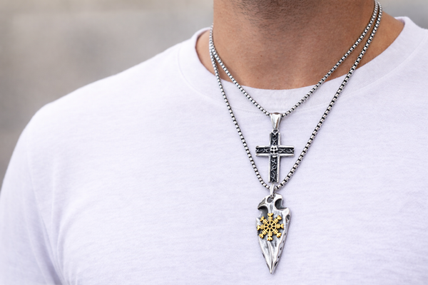 Man wearing layered stainless steel necklaces with cross and Viking arrowhead pendants on white T-shirt