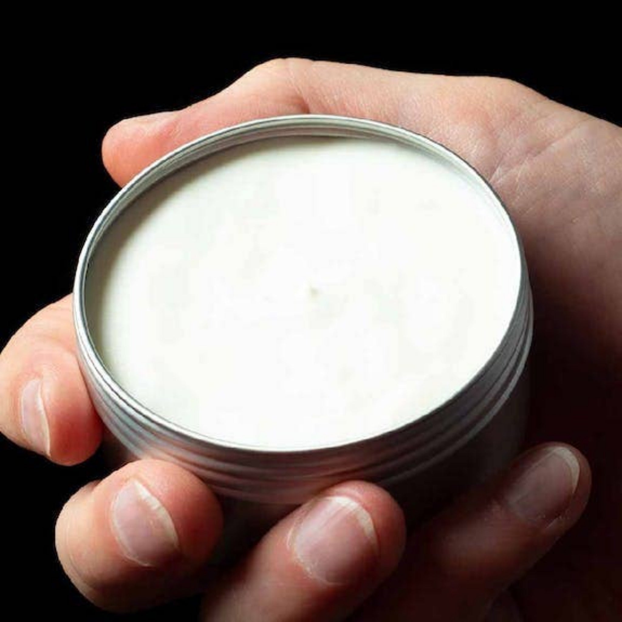 Open tin of Mo Bros Black Edition Beard Butter showing product texture in hand