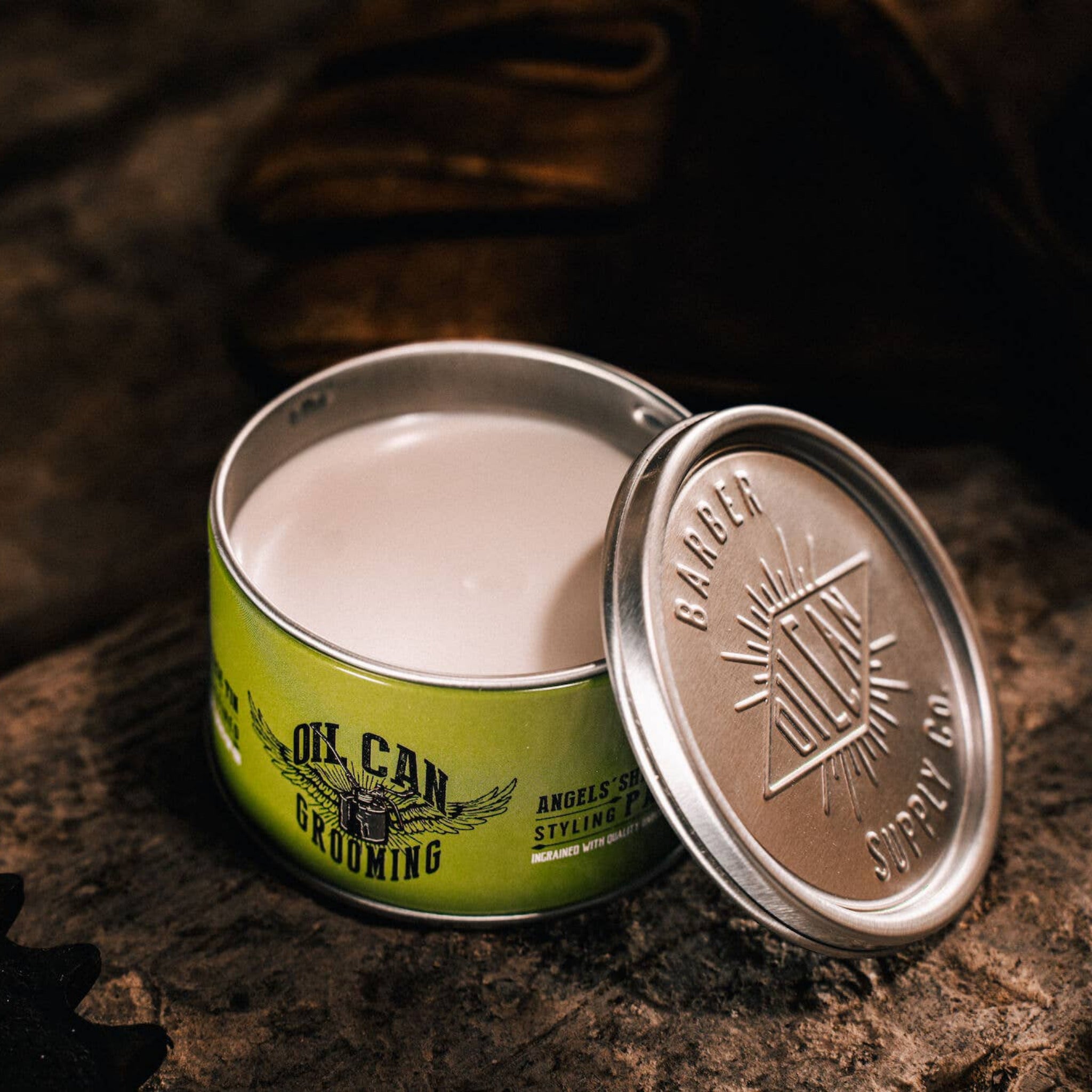 Oil Can Grooming Angels’ Share Styling Paste in moody barber shop lifestyle scene with open tin and styling product visible