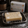 Paper Plane beard shampoo soap bar with lather in dark soap dish and boxed bar in rustic masculine bathroom setting