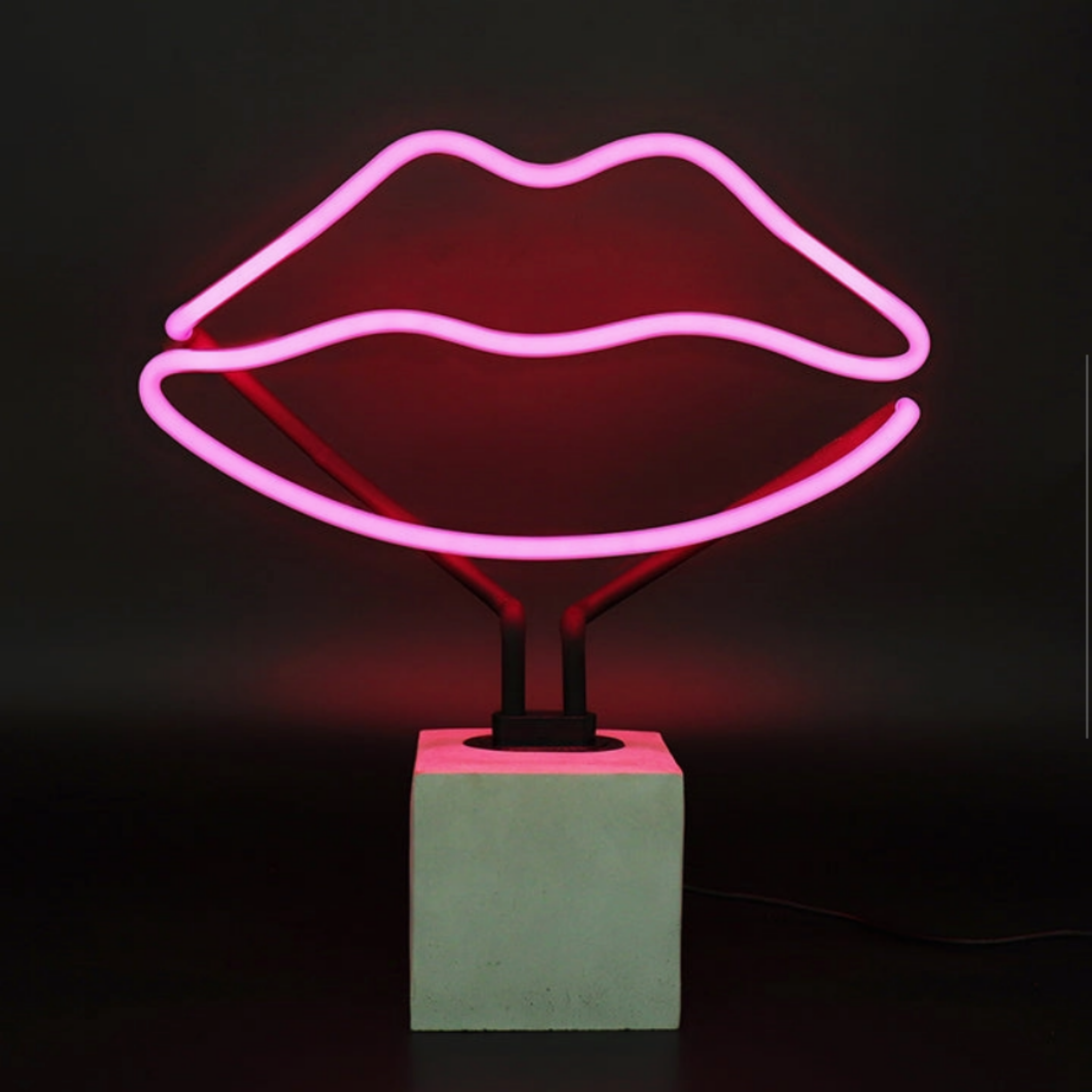 Pink lips neon lamp glowing on a concrete effect base against a dark background