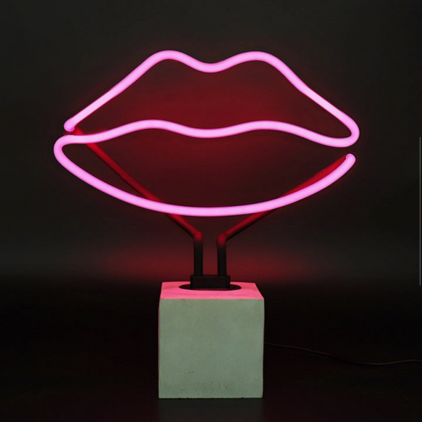 Pink lips neon lamp glowing on a concrete effect base against a dark background