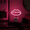 Pink lips neon lamp glowing beside books and speaker in a moody interior setting