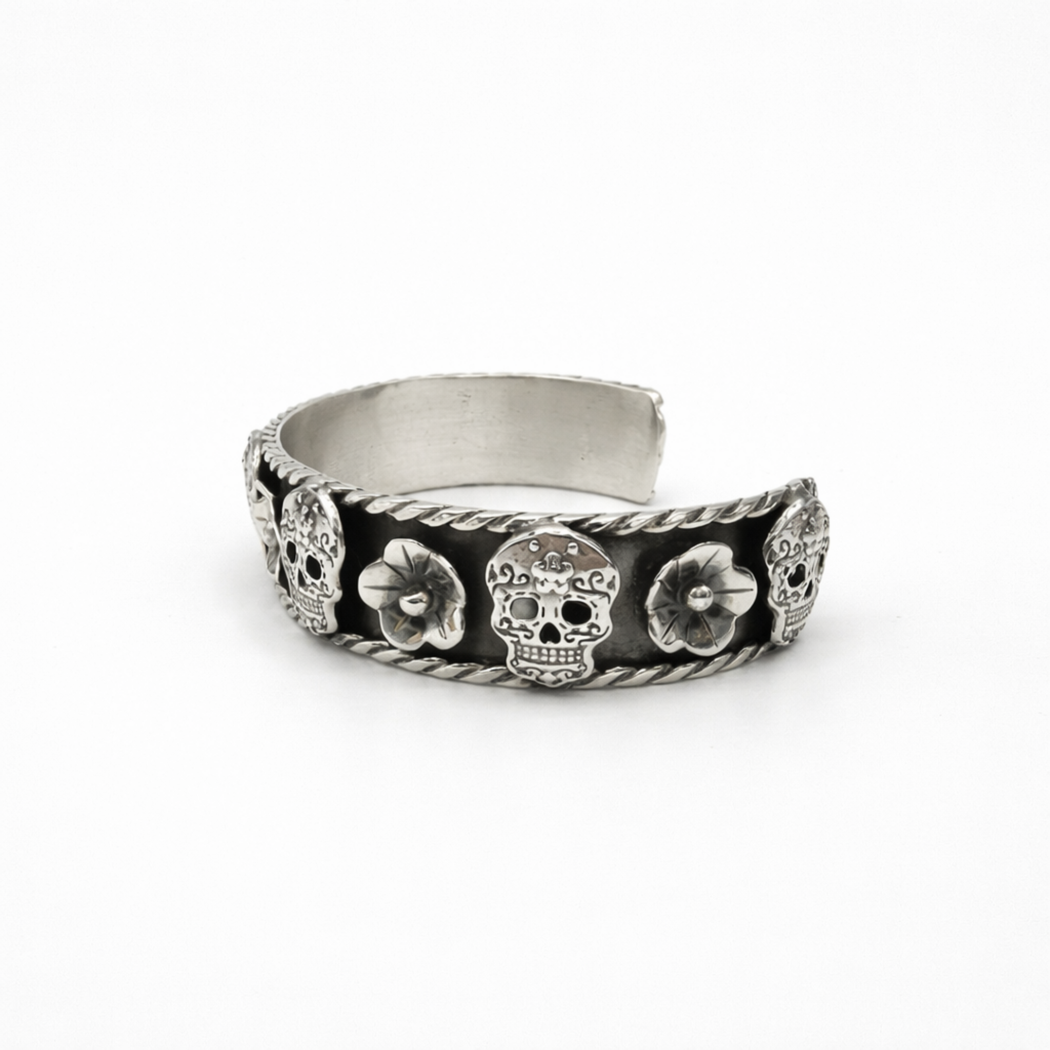 Sterling silver cuff bracelet with skull and flower design and oxidised finish angled view on white background