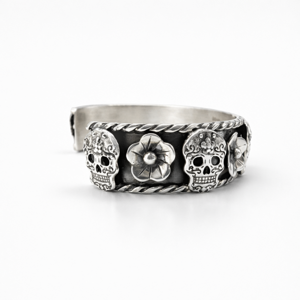 Sterling silver cuff bracelet with skull and flower design and oxidised finish on white background, side close-up view