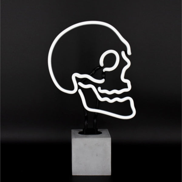 White skull neon lamp on concrete effect base against a dark background